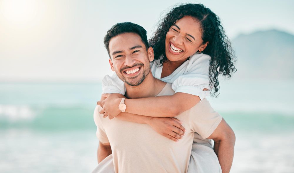 Man giving a woman a piggyback ride while laughing together on the beach