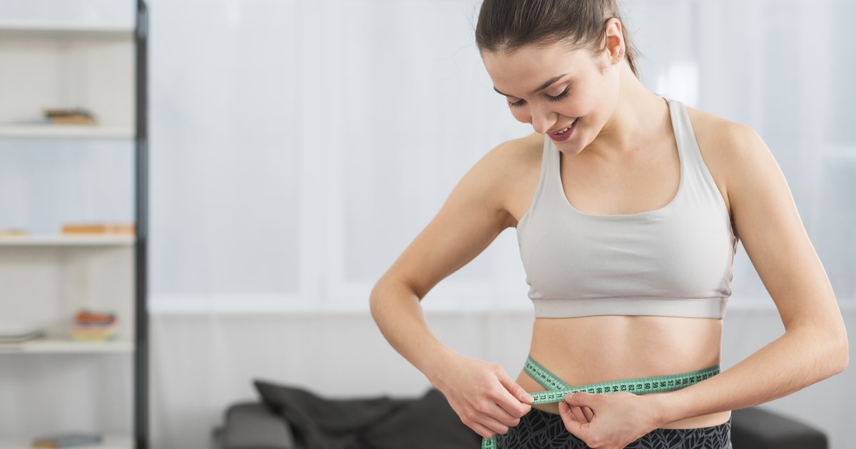 Woman in activewear measuring her waist with a tape measure